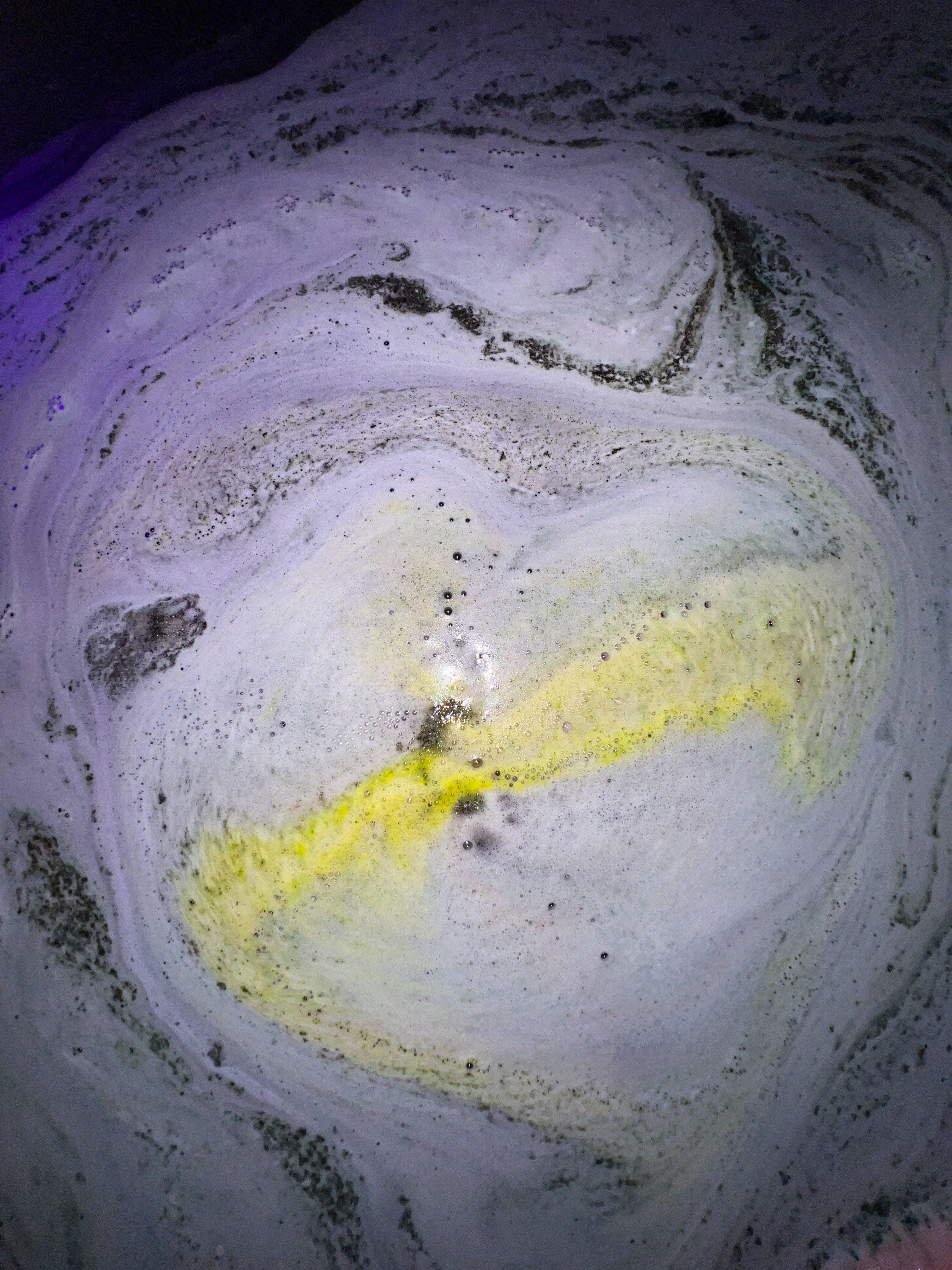 Close-up of a dissolved bath bomb swirling pattern with yellow and white colors on a dark background