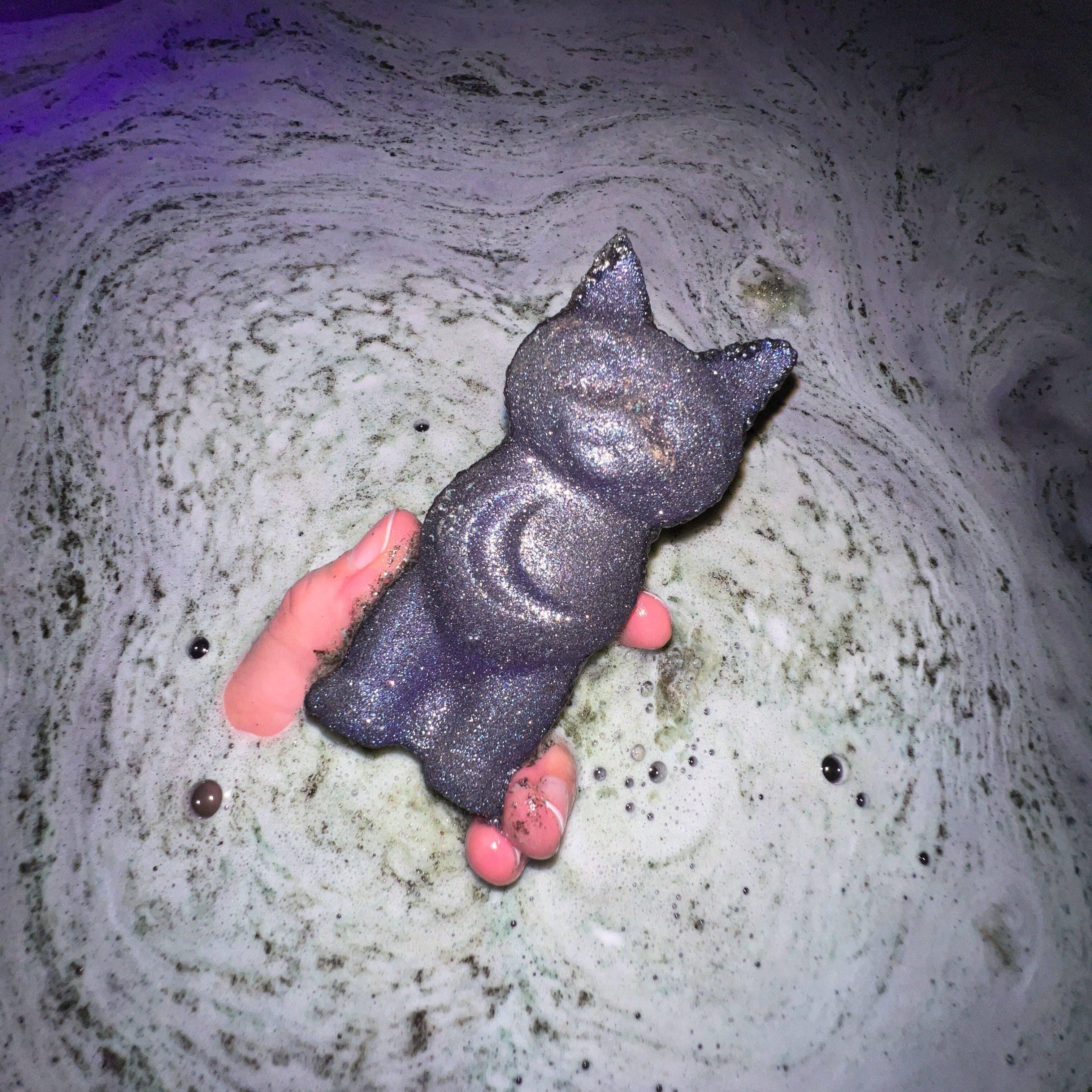 Person holding a cat-shaped bath bomb in a bathtub as it dissolves.