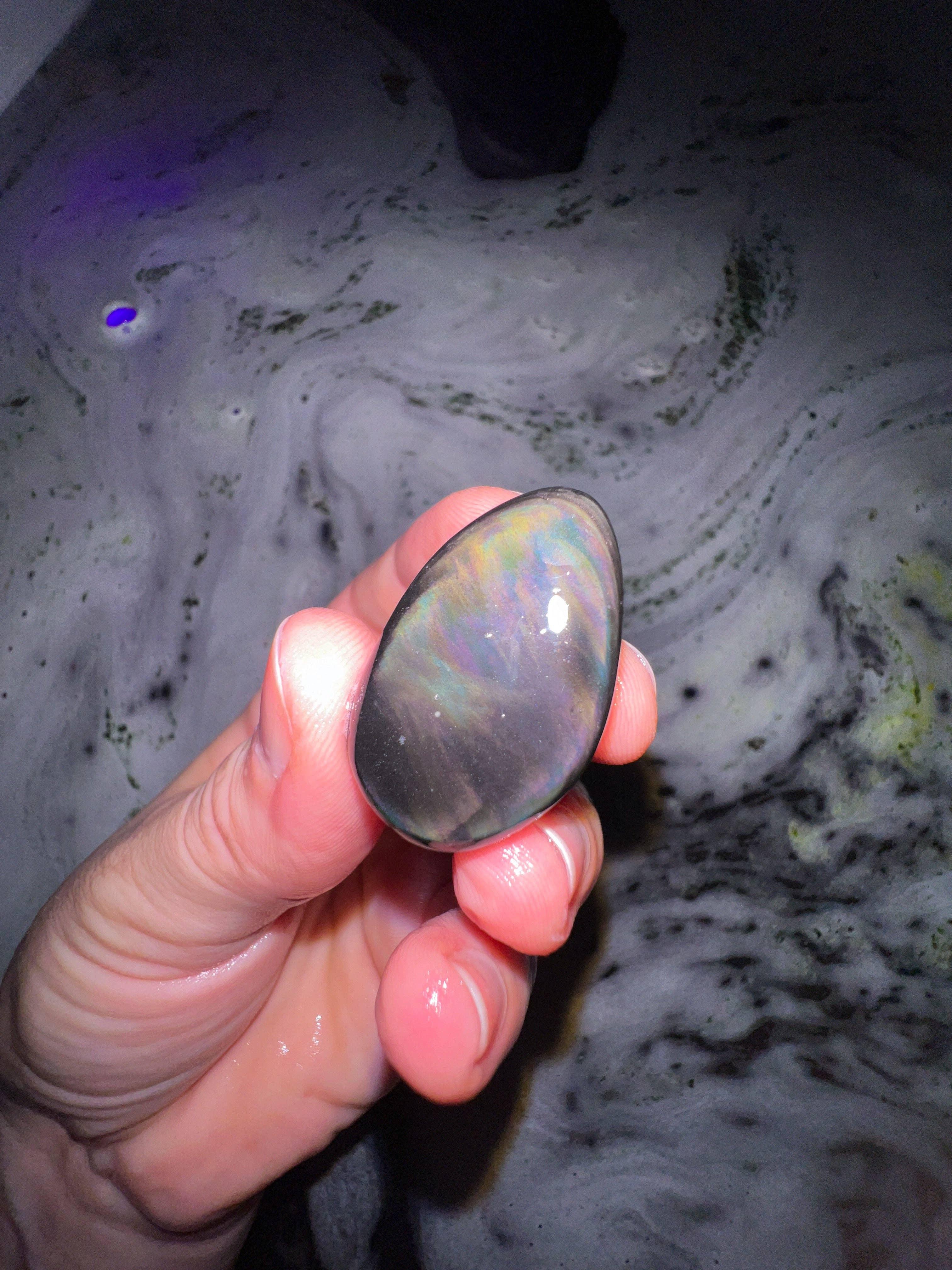 Hand holding a colorful stone against a swirling liquid background